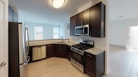 This two-story residence in Bayonne, NJ offers a well-designed layout across a generous footprint, combining modern finishes with a clean, contemporary aesthetic. The main living area features light-toned hardwood-style flooring and an open floor plan that flows seamlessly from the living space to the kitchen. Sliding glass doors allow abundant natural light to fill the room while providing access to outdoor views. The kitchen is appointed with dark espresso cabinetry, granite countertops, a subway tile backsplash, and a full suite of stainless steel appliances, including a gas range, built-in microwave, and dishwasher.

The three bedrooms are carpeted in a neutral grey tone and receive ample natural light through blinded windows. The primary bedroom is notably spacious, with dual windows overlooking the surrounding neighborhood. Each of the three bathrooms is finished consistently, featuring granite-topped vanities with dark cabinetry and tile flooring. One bathroom includes a walk-in glass shower, while another offers a full soaking tub with shower combination. Throughout, crisp white walls and bright flush-mount lighting contribute to a clean, move-in-ready ambiance.