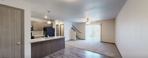 This two-story home offers a practical and well-appointed layout designed for comfortable everyday living. The main level features an open-concept living area with plush carpeting, a ceiling fan with light fixture, and a large sliding glass door fitted with vertical blinds that allows natural light to flow in and provides outdoor views. A staircase connects the two floors from within the living space. The kitchen is equipped with a peninsula island featuring a built-in sink, pendant lighting, medium-toned cabinetry, laminate countertops, and black appliances including a range, microwave, and refrigerator, all set on durable wood-style flooring. A half bathroom on the main level includes a dark wood vanity with a light countertop and wood-style flooring. Upstairs, multiple carpeted bedrooms each feature windows that bring in natural light, textured ceilings, and ample space. A full bathroom serves the upper level, complete with a single-sink vanity with dark cabinetry, a combination tub and shower, and wood-style flooring. A dedicated laundry area houses a full-size top-loading washer and dryer with an overhead wire shelving rack. The attached two-car garage provides additional storage and parking space with an automatic door opener.