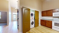 Located at 5 E Columbia Ave in Champaign, Illinois, this single-story unit is thoughtfully designed with a cohesive aesthetic throughout. Light-toned hardwood flooring extends across the main living areas, complementing the warm, neutral wall tones and creating a bright, welcoming atmosphere. Notably tall ceilings amplify the sense of openness in the hallway and main living spaces, where chandelier light fixtures add a refined touch.

The layout flows from an airy corridor into distinct living areas, with French doors at the end of the hall inviting natural light and providing access to an outdoor space. One carpeted bedroom features a generously sized walk-in closet with built-in shelving and hanging rods, offering ample storage. An additional room with hardwood flooring and a chandelier offers flexible use potential.

The bathroom is finished with classic white hexagonal tile flooring, sage-green walls, a walk-in shower with dark-framed glass doors, a pedestal sink, a wood-toned vanity with drawers, and an illuminated mirror. A dedicated laundry area includes a stacked washer and dryer tucked behind arched panel doors, alongside wood cabinetry providing extra storage. Overall, the space balances practicality with clean, comfortable design.
