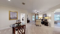 This single-floor residence offers a thoughtfully designed open-concept layout that seamlessly connects the living, dining, and kitchen areas. The spacious living room is anchored by plush wall-to-wall carpeting, elegant crown molding, and a ceiling fan, with multiple windows dressed in draped curtains that invite natural light. An arched passageway connects the living area to the bedroom wing, adding a refined architectural detail to the interior.

The dining area accommodates a round glass-top table and is complemented by a display cabinet and framed artwork, creating an intimate yet functional space. The kitchen features rich dark wood cabinetry, light granite countertops, a tile backsplash, stainless steel appliances, and durable tile flooring — combining style with practicality.

The bedrooms are serene and well-lit, each with carpeted floors, ceiling fans, and windows with blinds offering privacy and natural light. The bathroom is clean and functional, equipped with a walk-in shower with sliding glass doors, a vanity with dark wood cabinetry, and tile flooring that matches the kitchen.

Throughout the residence, a neutral warm color palette, crown molding, and consistent architectural details create a cohesive and comfortable living environment.
