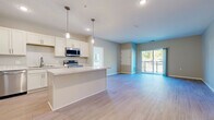 Located at 1920 Old Main St S in Cambridge, Minnesota, this thoughtfully designed single-floor residence offers three bedrooms and two bathrooms within a well-appointed, modern layout. The open-concept living area seamlessly connects the kitchen and living room, creating a bright and airy atmosphere enhanced by light wood-look flooring throughout the main areas. The kitchen is a standout feature, showcasing crisp white shaker cabinetry, a center island with a light stone-look countertop, pendant lighting, and a full suite of stainless steel appliances including a refrigerator, range, microwave, and dishwasher. The living room flows naturally toward a sliding glass door that opens to a private balcony, offering pleasant outdoor views and natural light. The bedrooms are comfortably sized, with soft carpeting underfoot, neutral tones, and generous closet space—including a dedicated walk-in closet with built-in shelving adjacent to one of the bathrooms. Both bathrooms feature light tile flooring, tub-shower combinations, and clean, contemporary fixtures. The overall aesthetic is cohesive and modern, with a neutral palette of whites, grays, and warm beiges that creates a calm, inviting ambiance throughout the home.