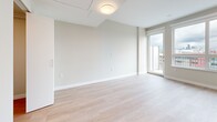 Located on the 7th floor at 2453 Renfrew St in Vancouver's Renfrew-Collingwood neighbourhood, this compact and efficiently designed studio unit offers a clean, modern aesthetic throughout. The open-concept layout maximizes the available floor area, with light-toned wide-plank flooring running continuously through the main living and kitchen spaces, creating a sense of warmth and cohesion.

The kitchen is well-appointed with two-tone cabinetry — crisp white upper cabinets extending to the ceiling paired with soft grey lower cabinets — complemented by white quartz countertops and a full suite of stainless steel appliances, including a range, built-in microwave, dishwasher, and refrigerator. A large window floods the kitchen with natural light and frames open city views, with direct access to a private balcony that extends the living space outdoors.

The main living area is bright and airy, with neutral beige walls, recessed lighting, and a sliding door leading to the balcony, further enhancing the sense of openness and connection to the outdoors.

The bathroom is finished to a high standard, featuring large-format grey marble-look floor tiles, a white quartz vanity with grey cabinetry, a mirrored medicine cabinet, and a full soaker tub with overhead shower. The all-white walls and recessed lighting contribute to a clean, spa-like atmosphere. A hallway connects all areas of the unit efficiently.