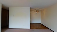This single-floor space offers a straightforward and functional layout designed with simplicity in mind. The interior is characterized by crisp white walls that create a bright, neutral backdrop throughout, lending the space a clean and airy feel. A partial dividing wall adds a subtle sense of separation between areas while maintaining an open flow within the floor plan.

The flooring transitions between materials, with rich hardwood floors visible in the main area, adding warmth and a classic touch to the space. A ceiling fan with a wooden blade design and an integrated light fixture is centrally positioned, providing both air circulation and ambient lighting to the room.

The overall ambiance is understated and practical, with a minimalist aesthetic that leaves room for a variety of furnishing styles and personal touches. The neutral color palette and simple architectural details make this space highly adaptable, whether for residential or other uses. The layout suggests a versatile living area that can easily be configured to suit different needs.