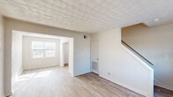 Located at 3715 George Washington Hwy in Portsmouth, Virginia, this two-story residence offers a practical and functional layout spread across two levels. The main floor features light wood-look flooring throughout the living and entry areas, creating a clean and cohesive aesthetic. A textured ceiling adds visual interest to the main living space, which benefits from multiple windows that invite natural light and provide views of the surrounding greenery. An interior staircase connects the main level to the upper floor, and a door from the kitchen provides convenient secondary access to the exterior. The kitchen is equipped with warm wood cabinetry, a white electric range, and light countertops, with a window above offering additional natural light. The upper level transitions to soft carpeted flooring throughout the bedrooms. Each bedroom is well-proportioned, with neutral walls, textured ceilings, and windows that frame outdoor views. Closet space is present in the upper-level rooms, enhancing storage options. Throughout the home, a neutral color palette of whites and warm beiges creates a bright, airy atmosphere. The overall design is straightforward and move-in ready, offering comfortable living in a residential Portsmouth neighborhood.