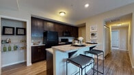 Located at Kenmore Crossing in Marysville, Ohio, this single-floor residence offers a well-designed layout that balances functionality and comfort throughout. The kitchen is a standout feature, showcasing rich dark espresso cabinetry extending to the ceiling, granite-style countertops, and black appliances including a refrigerator, range, and built-in microwave. A peninsula with bar seating provides a casual dining option and separates the kitchen from the living area. A dedicated pantry with open wire shelving adds convenient storage. Hardwood-style flooring flows through the kitchen and main living spaces, lending warmth and continuity. The living room is bright and inviting, highlighted by sliding glass doors that open to a private balcony, filling the space with natural light. The bedrooms are carpeted for comfort, with neutral tones and windows that offer outdoor views. One bedroom features dual closets, providing ample storage. The bathrooms are finished with tile flooring, dark vanity cabinetry, granite-style counters, and well-lit mirrors. Throughout the residence, a cohesive neutral color palette and consistent finishes create a clean, modern aesthetic that is both practical and welcoming.