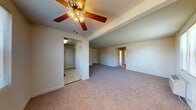 This single-floor unit offers a practical and functional layout across several interconnected rooms. The main living area is generously sized, featuring neutral-toned wall-to-wall carpeting and a ceiling fan with a light fixture overhead. A raised ceiling detail adds visual depth to the space. The open layout connects to additional rooms via clearly defined doorways, providing a straightforward flow throughout the unit.

The kitchen is equipped with warm honey-toned wood cabinetry offering ample upper and lower storage, dark laminate countertops, a stainless steel sink beneath a window that allows natural light in, and a gas range with an overhead ventilation hood. A refrigerator is also present.

The bathroom features classic white tile work, a tub-shower combination, a single vanity with a wall-mounted mirror, and a window providing natural ventilation. The mosaic tile flooring adds a traditional touch.

The bedrooms are carpeted and each includes a ceiling fan, a closet with a hanging rod, natural light from windows, and a wall-mounted HVAC unit. The neutral walls throughout the unit provide a clean, move-in-ready canvas. White trim and panel-style doors are consistent features across all rooms.