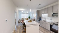 Located at 621 Glen Manor Trail in Knightdale, NC, this well-appointed 2-bedroom, 3-bathroom single-floor residence offers a thoughtfully designed open-concept layout. The kitchen is a standout feature, showcasing gray shaker cabinetry, granite countertops, a subway tile backsplash, and a full suite of stainless steel appliances including a dishwasher, microwave, range, and refrigerator. A large granite-topped island with pendant lighting above serves as both a prep space and casual dining area, flowing seamlessly into the combined dining and living room. The living area is bright and welcoming, with natural light streaming through sheer-draped windows and a ceiling fan overhead. Wood-style plank flooring runs throughout the home, adding warmth and continuity. The primary bedroom is a comfortable retreat, while additional bedrooms offer versatile space. The bathrooms are finished with granite vanities, gray cabinetry, and modern fixtures; one bath features a double vanity and glass-enclosed shower. A dedicated laundry room houses a full-size washer and dryer with wire shelving above. Two closets with wire shelving systems provide ample storage. The home combines a neutral, modern palette with functional finishes for a clean, cohesive living environment.