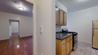 Located at 2 Osborne Terrace in Newark, NJ, this one-bedroom, one-bathroom unit offers a practical and well-organized single-floor layout. Warm hardwood flooring flows throughout the living room, hallways, and bedroom, lending a cohesive and inviting character to the space. The living room is generously proportioned, featuring neutral walls and a hallway that connects seamlessly to the rest of the unit. The spacious primary bedroom benefits from a large multi-pane window that draws in natural light and provides views of the surrounding neighborhood, complemented by a classic cast-iron radiator for reliable heating. The kitchen is efficiently designed with warm-toned wood cabinetry, dark granite-style countertops, a stainless steel refrigerator, and a gas range with overhead storage, all set on light tile flooring. The bathroom features full floor-to-ceiling earth-toned tile surrounding a white soaking bathtub and shower combination, with a window above for natural ventilation. Two hallways connect the rooms, ensuring a smooth and functional flow throughout the unit. The overall ambiance is clean, understated, and move-in ready.
