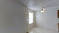 This single-floor space offers a straightforward and functional layout with a clean, neutral aesthetic. The interior is characterized by crisp white walls, including a distinctive vertical panel-style wall accent that adds a subtle architectural detail to the room. The textured popcorn ceiling adds dimension overhead, while a ceiling fan with a built-in light fixture provides both air circulation and ambient lighting. Natural light filters into the space through a window fitted with white horizontal blinds, casting a bright and airy feel across the light-toned tile flooring. The room's simple, uncluttered design makes it highly versatile and easy to personalize. The overall ambiance is calm and understated, with a neutral color palette of whites and soft off-whites that creates a sense of openness. The space is well-suited for a variety of uses, offering a blank canvas for customization. Its single-floor layout ensures easy accessibility and seamless flow throughout, making it a practical and comfortable environment for everyday living.