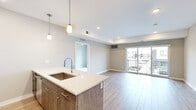 This modern 2-bedroom, 1-bathroom residence in Troy, Michigan offers a thoughtfully designed open-concept layout with contemporary finishes throughout. The combined kitchen and living area serves as the heart of the home, anchored by a sleek kitchen island with a white quartz countertop, an undermount sink, and pendant lighting overhead. The kitchen is fully equipped with stainless steel appliances, including a gas range, microwave, and refrigerator, complemented by wood-toned cabinetry. Light wood-style flooring extends throughout the main living areas, enhancing the bright and airy atmosphere. The living room opens directly to a private balcony through sliding glass doors, allowing natural light to fill the space and providing outdoor views of the surrounding community. Both bedrooms feature plush carpeting and large windows that invite natural light, with the second bedroom offering generous closet storage. The full bathroom is finished with large-format tile flooring, a wood-toned vanity with quartz countertop, and a walk-in shower. A dedicated closet near the entryway provides additional storage. Clean neutral tones and modern fixtures throughout create a cohesive, contemporary aesthetic.