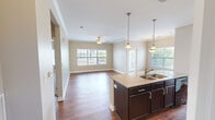 Located at 7300 Sir Walter Way in Knoxville, Tennessee, this well-appointed 2-bedroom, 2-bathroom residence offers a thoughtfully designed single-floor layout. The open-concept living area serves as the heart of the home, where rich hardwood-style flooring flows seamlessly from the kitchen through the dining and living spaces. The kitchen is equipped with dark cabinetry, granite countertops, a central island with a built-in sink, pendant lighting, track lighting, and black appliances including a refrigerator and range. Large windows in the living room and dining area invite abundant natural light and provide views of the surrounding community. Crown molding adds a refined architectural detail throughout the main living areas. The dining room features a classic overhead light fixture and its own window with outdoor views. Both bedrooms are carpeted and finished with neutral tones, offering a comfortable, quiet retreat with ceiling fans and ample natural light. The primary bathroom includes both a soaking tub and a separate glass-enclosed shower, finished with tile flooring and granite countertops. A dedicated laundry room with a full-size washer and dryer and built-in shelving adds everyday convenience. Two closets and a hallway complete the efficient and functional floor plan.