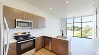 Located at 217 E Campbell St in Edmond, Oklahoma, this thoughtfully designed one-bedroom, two-bathroom residence offers a contemporary living experience on a single floor. The open-concept layout maximizes the use of space, creating a cohesive flow between the living and kitchen areas. The kitchen is a standout feature, boasting rich dark wood cabinetry, a white quartz peninsula with an undermount sink and matte black faucet, subway tile backsplash, and a full suite of stainless steel appliances including a refrigerator, range, and microwave. Light wood-style flooring ties the kitchen and main living areas together seamlessly. The bedroom is generously proportioned, featuring plush carpet flooring and floor-to-ceiling black-framed windows that flood the room with natural light and offer outdoor views. Both bathrooms are finished to a high standard — one includes a floating wood vanity with a framed mirror, matte black fixtures, wood-look tile flooring, and a marble-tiled shower with a sliding barn-style door, complemented by a large window with garden views. A walk-in closet with built-in wire shelving provides practical storage. Clean white walls, five-panel interior doors, and modern hardware complete the refined, contemporary aesthetic throughout.