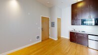 Located on the fourth floor at 5043 Brooklyn Ave NE in Seattle's University District, Unit 407 is a thoughtfully designed studio that makes efficient use of its compact footprint. The main living area features warm-toned bamboo hardwood flooring that runs throughout, lending a clean and cohesive look to the space. Neutral gray walls and white trim create a bright, minimalist aesthetic, while a window with vertical blinds allows natural light to fill the room.

The kitchenette is neatly integrated along one wall, outfitted with rich dark wood cabinetry, a compact electric range, a sink, and an over-the-range microwave — providing essential cooking functionality without compromising on living space. An electrical panel is conveniently recessed into the wall near the entry.

The bathroom is accessible directly from the main living area and features tile flooring, a wall-mounted sink, a toilet, and a mirrored medicine cabinet, keeping the layout practical and organized.

The unit's tall ceilings contribute to an open, airy feel despite the studio format. A fire alarm and safety systems are visibly installed, reflecting attention to building safety standards. Overall, this unit offers a clean, move-in-ready space well-suited for efficient urban living in Seattle.