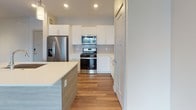 This single-floor residence at 129 Parker St in Maynard, Massachusetts offers a contemporary, well-appointed layout designed for comfortable living. The open-concept living and kitchen area is anchored by rich hardwood-style flooring that runs throughout the main living spaces, creating a cohesive and modern aesthetic. Large sliding glass doors in the living area invite natural light and provide access to an outdoor balcony, offering views of the surrounding neighborhood.

The kitchen is a standout feature, equipped with white shaker-style cabinetry, a subway tile backsplash, stainless steel appliances including a refrigerator with ice maker, a gas range, and a microwave. A central island with a light wood panel base and white quartz countertop provides additional prep space and pendant lighting overhead adds a refined touch.

The bedrooms feature plush carpeting, ceiling fans, and windows that bring in natural light with neighborhood views. One bedroom includes a walk-in closet with built-in shelving, offering generous storage. The bathroom is finished with wood-toned cabinetry, a white quartz vanity top, a framed mirror, and a glass-enclosed shower, all set on hardwood-style flooring. Throughout, the unit maintains a clean, neutral palette that lends a bright and welcoming ambiance.
