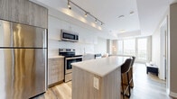 Located in Ottawa's vibrant Wellington West neighbourhood, this modern 1-bedroom, 2-bathroom unit offers a thoughtfully designed open-concept layout finished with warm wood-look vinyl flooring and a neutral colour palette throughout. The kitchen is a standout feature, equipped with stainless steel appliances including a range, over-the-range microwave, and dishwasher, complemented by light wood cabinetry, a white subway tile backsplash, and a central island with bar seating — ideal for both cooking and casual dining. Track lighting overhead adds a contemporary touch. The living area flows naturally from the kitchen toward large floor-to-ceiling windows that invite abundant natural light and offer open outdoor views of the surrounding cityscape. The bedroom is a comfortable retreat, featuring large windows with the same expansive views, wood-look flooring, and a clean, minimalist aesthetic. The unit includes two bathrooms: one with a soaker tub and white tile surround, and a second featuring a glass-enclosed walk-in shower — both finished with light tile, wood-tone vanities, and modern fixtures. Hallways with mirrored closet doors and a dedicated closet add practical storage. The overall ambiance is bright, clean, and contemporary.