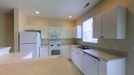 Located at 3900 Suffolk Dr in Dublin, Ohio, this two-story home offers a clean, functional layout across two well-organized floors. The kitchen is thoughtfully designed with ample white cabinetry extending to the ceiling, generous counter space, and a full suite of white appliances including a refrigerator, electric range, built-in microwave, and dishwasher. A double basin sink sits beneath a window that brings in natural light, keeping the workspace bright and welcoming. Recessed lighting and light-toned countertops contribute to the kitchen's crisp, airy atmosphere. The adjacent living area is open and inviting, featuring plush wall-to-wall carpeting and recessed ceiling lights that provide consistent, even illumination throughout the space. Neutral-toned walls offer a versatile backdrop suited to a variety of interior styles. A staircase with white railings leads to the upper floor, adding a sense of vertical openness to the main level. A front entry door with sidelights allows additional natural light into the living area, connecting the interior to the outdoors. Together, these spaces form a cohesive and comfortable home well-suited for everyday living in the Dublin community.