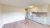 This efficiently designed one-bedroom, one-bathroom unit offers a well-organized layout across a single floor, making practical use of every square foot. Light-toned luxury vinyl plank flooring runs consistently throughout the space, creating a clean, cohesive aesthetic that visually opens the interior.

The kitchen is a standout feature, showcasing updated white shaker-style cabinetry with brushed gold hardware, a light quartz countertop, and a classic grey subway tile backsplash. A single-basin undermount sink with a modern faucet and a white electric range complete the functional cooking space. Natural light enters through a window adjacent to the kitchen area, offering views of the surrounding neighborhood.

The living room provides an open, neutral canvas with warm beige walls, white baseboards, and a textured ceiling. A window allows additional natural light to brighten the space. The bedroom is a comfortable, well-proportioned room featuring a window with outdoor views, a baseboard heater, and the same consistent flooring. The bathroom is finished in a clean, all-white palette with a shower-tub combination, a single vanity with storage, and a small window for ventilation. Overall, the unit presents a bright, updated, and functional living environment.