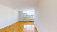 Located on the 6th floor at 145 St George Street in Toronto's desirable Annex neighbourhood, this unit offers a well-organized, single-level layout comprising a living room and two bathrooms. Throughout the space, warm-toned parquet flooring laid in a classic basket-weave pattern adds a timeless character to the interior. The living area is bright and open, benefiting from a large floor-to-ceiling window wall that invites an abundance of natural light and frames views of the surrounding Toronto cityscape. The clean white walls and smooth ceilings contribute to a fresh, airy ambiance. The kitchen is efficiently designed, featuring white cabinetry and standard appliances, making practical use of the available space. A walk-in closet provides dedicated storage, complete with a hanging rod and open shelving. The bathroom is finished with neutral beige ceramic wall tiles surrounding a full-sized soaking tub and shower combination, complemented by white fixtures and a vanity. The overall design is clean and functional, with a neutral palette that provides a versatile backdrop. The unit's location within the vibrant St. George corridor offers convenient access to the University of Toronto, transit, parks, and a wide range of urban amenities.
