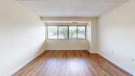 Located on the third floor at 2405 Whitney Ave in Hamden, Connecticut, Unit 307 is a thoughtfully designed one-bedroom, one-bathroom residence that makes efficient use of its single-floor layout. Warm hardwood-style flooring runs throughout the unit, creating a cohesive and inviting atmosphere from room to room.

The combined kitchen and living area forms the heart of the unit. The kitchen is outfitted with white cabinetry, granite-look countertops, a white electric range, a dishwasher, and a tiled backsplash, all contributing to a clean, functional aesthetic. The adjacent living area offers generous open space, with soft neutral walls and tile ceiling panels that complement the light-toned interior.

The bedroom is a comfortable, well-proportioned space featuring a wide horizontal window fitted with blinds, allowing natural light and outdoor views of the surrounding greenery. A set of double sliding closet doors provides ample storage, completing the room's practical appeal.

The bathroom features a full soaking tub and shower combination with a clean white surround and built-in shelving niches, maintaining the unit's consistent, tidy design language.

Throughout the residence, clean white trim, neutral wall tones, and consistent flooring create a bright, move-in-ready environment well suited for comfortable everyday living.
