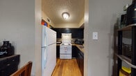 This single-floor residence offers a well-organized layout that connects living, dining, and sleeping spaces through a continuous stretch of warm hardwood flooring. The kitchen is efficiently designed in a galley-style configuration, featuring dark cabinetry with ample upper and lower storage, granite-look countertops, white appliances including a full-size refrigerator and electric range with overhead ventilation, and a sink tucked neatly at the end of the counter. A textured ceiling adds character throughout the home. The living area provides a comfortable gathering space with natural light streaming in through windows fitted with blinds, and flows easily toward the dining area and kitchen. The primary bedroom accommodates a full-size bed and multiple storage pieces, benefits from a ceiling fan, a window with natural light, and offers enough space for additional furnishings. The second bedroom is a cozy, well-proportioned room with its own window and ceiling fan. The bathroom features a dark vanity with a granite-look countertop, a round framed mirror, and a shower-tub combination with a curtain enclosure, all set over the same hardwood flooring that runs through the rest of the home. The overall ambiance is practical and comfortable, with consistent finishes tying each room together cohesively.