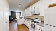 Located at 179 Emmaus Rd in Marysville, Ohio, this well-designed one-bedroom, one-bathroom unit offers a thoughtful layout that maximizes every square foot of its compact footprint. Warm hardwood-style flooring runs throughout, providing a cohesive and inviting aesthetic across all rooms.

The combined kitchen and living area serves as the heart of the unit. The kitchen features crisp white shaker cabinets, grey laminate countertops, a peninsula with a built-in sink, and a full suite of white appliances including a range, microwave, dishwasher, and refrigerator. Recessed lighting and a barn-style entry door add contemporary touches. The adjoining living space is accented by a bold charcoal feature wall and a window fitted with horizontal blinds, allowing natural light while maintaining privacy.

The bedroom is a calm retreat, characterized by a two-tone wall design with a soft grey accent wall, a window overlooking greenery, and a closet. Recessed lighting and warm wood furnishings contribute to a comfortable, functional atmosphere.

The bathroom is cleanly finished with light-toned walls, wood-style flooring, a white vanity with grey countertop, and black hardware accents. Its open doorway connects directly to the bedroom, enhancing the flow between spaces. Overall, the unit presents a modern, move-in-ready interior with consistent, tasteful design choices throughout.