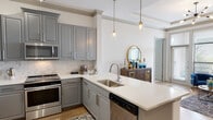 This single-floor residence offers a thoughtfully designed open-concept layout that seamlessly connects the kitchen, dining, and living areas. The kitchen is a standout feature, showcasing gray shaker-style cabinetry with crown molding, white quartz countertops, a marble-inspired tile backsplash, and a full suite of stainless steel appliances including a French door refrigerator, slide-in range, built-in microwave, and dishwasher. A peninsula island with an undermount sink and pendant lighting above adds both function and style. Warm hardwood-style flooring extends throughout the main living areas.

The living room impresses with a coffered tray ceiling, crown molding, and a sputnik-style chandelier that anchors the space. Bedrooms feature plush carpet flooring and calming blue accent walls, with natural light filtering through horizontal blinds. The primary bathroom includes a granite-topped vanity with gray cabinetry, large-format tile flooring, and a soaking tub with subway tile surround. A second bathroom mirrors the same refined finishes. Track lighting, crown molding, and consistent gray tones throughout create a cohesive, contemporary aesthetic.