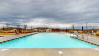 Located at 142 Patrick Murphy Dr in Morganton, North Carolina, this single-story community amenity facility offers a well-appointed outdoor recreational experience set against the backdrop of the Blue Ridge foothills. The centerpiece of the space is a generously sized swimming pool with clear, blue water, surrounded by an expansive concrete sundeck designed to accommodate ample lounge seating for relaxation and recreation.

The pool area is enclosed by warm wood-toned fencing that provides both privacy and a welcoming aesthetic, while landscaped borders with ornamental grasses and plantings add natural texture to the environment. Multiple lounge chairs and outdoor tables are positioned throughout the deck, offering comfortable spots for sunbathing or socializing.

A standout architectural feature of the facility is a prominent cylindrical brick silo tower flanking the main building entrance. This distinctive design element lends the space a character-rich, industrial-meets-rustic aesthetic. The building entry is accessed through double glass doors beneath a covered canopy, providing a clean and functional transition between the interior and the outdoor deck areas.

The surrounding community provides pleasant open views, and the facility's single-floor layout ensures easy, accessible navigation throughout. Overall, this amenity space delivers a practical and visually engaging environment tailored for community leisure and outdoor enjoyment.