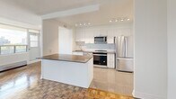 Located on the sixth floor at 15 Eva Rd in Toronto's Etobicoke neighbourhood, this one-bedroom suite offers a thoughtfully laid-out single-level floor plan. Classic parquet wood flooring runs throughout the living spaces, adding warmth and character to the bright, white-walled interior.

The kitchen is a standout feature, finished with crisp white cabinetry, a subway tile backsplash, dark countertops, and a full suite of stainless steel appliances including a range, over-the-range microwave, and French door refrigerator. A peninsula with additional counter space connects the kitchen to the living area, creating an open and functional flow ideal for cooking and entertaining. Light tile flooring anchors the kitchen zone.

The living room is generously proportioned, bathed in natural light from large floor-to-ceiling windows that frame open city views of the Toronto skyline and surrounding greenery. A baseboard heating unit runs along the window wall, ensuring comfort year-round.

The bedroom offers a comfortable, well-sized layout with the same warm parquet flooring, white walls, and two interior doors providing access to a closet and connecting hallway. The overall ambiance of the suite is clean, bright, and move-in ready, with a neutral palette that lends itself to a variety of personal styles.