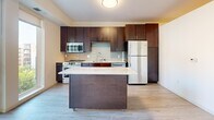 Located at 5310 W 16th St in St. Louis Park, MN, this one-bedroom, one-bathroom unit offers a thoughtfully designed single-floor layout that maximizes every inch of its compact footprint. The entrance opens into a clean hallway with light wood-style flooring and a louvered closet door, leading seamlessly through the space. The kitchen is a standout feature, showcasing rich dark cabinetry extending to the ceiling, a classic subway tile backsplash, stainless steel appliances including a range, built-in microwave, and refrigerator, and a central island topped with a polished granite surface. Floor-to-ceiling sliding glass doors flood the kitchen and living area with abundant natural light and provide direct access to a private balcony with open outdoor views. The bathroom is well-appointed with a full soaking tub and shower combination, a dark-framed vanity mirror, a white countertop sink, and light tile flooring that complements the bright, clean walls. The bedroom features neutral carpet flooring and crisp white walls, offering a calm and comfortable retreat. Throughout the unit, the consistent use of light tones and dark wood accents creates a modern, cohesive aesthetic.