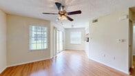 This efficiently designed single-floor unit offers a thoughtful layout across three distinct areas: a combined kitchen and living room, a full bathroom, and a closet. The open-plan living and kitchen area forms the heart of the unit, bathed in natural light from multiple windows with horizontal blinds and a sliding glass door that opens to an outdoor view. Light hardwood-style flooring runs throughout, complementing the neutral, warm-toned walls. A ceiling fan with an integrated light fixture adds both function and character to the living space, while a textured popcorn ceiling adds a classic touch overhead.

The kitchen is well-appointed with light wood cabinetry, dark speckled countertops, a double-basin sink, and black appliances including an electric range, over-the-range microwave, and refrigerator. A mosaic tile backsplash adds a subtle decorative accent. The space flows efficiently, with direct access to the rest of the unit.

The bathroom features a full tub-shower combination with clean white tile surround accented by a horizontal band of gray mosaic tile, lending a polished, classic aesthetic. A dedicated closet provides organized storage. Consistent hardwood-style flooring and neutral walls tie the entire unit together into a cohesive, functional living space.