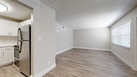 This single-floor unit presents a clean, contemporary aesthetic defined by light wood-look flooring and a consistent neutral color palette that extends throughout every room. The open layout connects the living area to the kitchen, which is outfitted with white cabinetry featuring brushed nickel hardware, quartz countertops, a stainless steel undermount sink with a high-arc faucet, and a full suite of stainless steel appliances including an electric range, over-the-range microwave, and refrigerator. The living and bedroom areas are generously sized, with textured ceilings, crisp white baseboards, and multiple windows fitted with blinds that allow natural light to filter in. A sliding glass door in one of the rooms leads to an outdoor area, further enhancing the sense of openness. The bathroom features a white vanity with quartz countertop, an undermount sink, brushed nickel fixtures, and a framed mirror with a multi-bulb vanity light. A walk-in closet provides practical storage. The overall ambiance is modern, clean, and move-in ready.