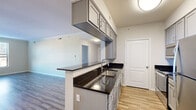 Located at 612-628 N New Ballas Rd in Creve Coeur, Missouri, this single-floor residence offers a thoughtfully designed layout that combines modern finishes with functional living spaces. The kitchen serves as a central highlight, featuring dark granite countertops, gray shaker-style cabinetry — including overhead storage — a stainless steel sink, and a full suite of stainless steel appliances including a refrigerator, range, and microwave. A peninsula with an overhang provides a natural transition into the open living area, which is finished with wood-style plank flooring and crown molding. Large windows in the living area allow generous natural light to filter in, offering views of the surrounding neighborhood. The bedrooms are carpeted and well-sized, each with windows that bring in additional daylight. The bathroom is clean and functional, featuring wood-style flooring, a full bathtub/shower combination, and neutral finishes throughout. A hallway connects the main living spaces, with a louvered closet door adding a classic touch. The overall design palette is light and neutral, with white walls and trim creating a bright, welcoming ambiance throughout the residence.