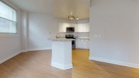 Located at 101 W Read St in Baltimore's Mount Vernon neighborhood, this single-floor residence offers a clean, modern aesthetic throughout. The open-concept kitchen is a standout feature, appointed with crisp white shaker cabinetry, granite countertops, and a full suite of stainless steel appliances including a range, over-the-range microwave, and dishwasher. A peninsula with a granite overhang provides casual seating and seamlessly connects the kitchen to the living area. Light hardwood flooring runs throughout the main living spaces, enhancing the bright, airy feel of the interior. The living and bedroom areas benefit from multiple windows dressed with horizontal blinds, inviting abundant natural light and offering views of the surrounding streetscape. Clean white walls and substantial baseboards lend a crisp, well-maintained character to each room. The bathroom is finished with neutral tile flooring, a white vanity, and a walk-in shower with chrome fixtures, maintaining the unit's consistent, modern style. The overall layout, as suggested by the floor plan, is efficiently organized and well-connected, making the space feel open and functional. This residence combines updated finishes with a practical single-level design in a prime Baltimore location.