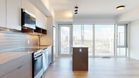 Located at 280 Montgomery St in Ottawa, Ontario, this thoughtfully designed studio unit offers a contemporary and efficient living experience. The open-concept layout seamlessly integrates the living, dining, and kitchen areas into a single bright and airy space. Light hardwood flooring runs throughout, complementing the clean white walls and modern track lighting overhead.

The kitchen is well-appointed with sleek grey cabinetry, warm wood open shelving, a tiled backsplash, stainless steel appliances including a range, dishwasher, refrigerator, and built-in microwave, as well as a central island that doubles as a dining and prep surface. Floor-to-ceiling windows and a glass balcony door flood the space with natural light and frame impressive panoramic views of the Ottawa skyline, making the most of the elevated position of the unit.

The bathroom features a glass-enclosed walk-in shower with crisp white vertical tile, grey tile accents, and matte black fixtures for a refined, modern aesthetic. The unit also includes a dedicated laundry area and a closet, adding practical storage and convenience. The overall ambiance is clean, contemporary, and efficient — ideal for those seeking a well-designed urban residence in Ottawa.