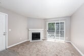 This single-floor residence offers a practical and comfortable layout designed for everyday living. The living room serves as the heart of the space, highlighted by a tile-surround fireplace and a large sliding glass door fitted with vertical blinds that flood the room with natural light and provide access to the outdoors. Neutral-toned carpet and warm beige walls create a welcoming atmosphere throughout.

The kitchen is open and functional, featuring white cabinetry, light countertops, a coil-burner electric range with overhead ventilation, and a refrigerator. A peninsula-style counter with a sink separates the kitchen from the adjoining living area, making the space feel connected and social.

The bedroom is generously proportioned, with plush carpet, a large window framing views of surrounding greenery, and a baseboard heater for year-round comfort. Clean white trim and neutral walls keep the room bright and versatile.

The bathroom is finished with light wood-look flooring, white cabinetry beneath a wide vanity countertop, a large mirror, and a well-lit vanity strip above. The overall design of the space is clean and understated, with consistent neutral tones and functional finishes that provide a solid foundation for personalization.