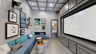 This dedicated theater space is thoughtfully designed to deliver an immersive entertainment experience without sacrificing style. The room is anchored by a large projection screen mounted within a sleek, built-in gray cabinetry unit that spans the far wall, providing both a polished focal point and integrated media storage. Overhead, a striking coffered ceiling with recessed lighting adds architectural depth and a refined aesthetic while contributing to the room's acoustics. The seating arrangement features a spacious teal sectional sofa that lines two walls, offering generous, comfortable viewing capacity. A set of industrial-style drum ottomans with metallic tops serve as flexible accent pieces and additional seating in the center of the room. The walls are adorned with a curated gallery of framed artwork, lending the space a creative and personalized atmosphere. Neutral gray tones throughout — from the walls and cabinetry to the polished concrete-style flooring — create a cohesive, contemporary palette. A glass-paneled interior door adds a sophisticated touch while maintaining visual openness. In-ceiling speakers are also visible, pointing to a fully integrated audio-visual setup built for a true cinematic experience.