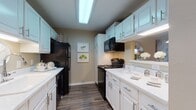 This single-story residence offers a well-organized layout that balances functionality and comfort throughout its connected living spaces. The galley-style kitchen is a standout feature, showcasing crisp white cabinetry with brushed silver hardware extending from floor to ceiling, providing generous storage. Light-toned countertops contrast neatly with black appliances, including an electric range, over-the-range microwave, and refrigerator. Wood-look flooring runs throughout the kitchen and continues into the adjacent dining area, which is illuminated by a pendant light and features a pass-through opening connecting it to the kitchen. The living room benefits from natural light streaming through a set of French doors that open to an outdoor space, creating a bright and welcoming atmosphere. Two bedrooms are finished with plush carpeting and ceiling fans; each room offers closet storage and windows with outdoor views. The full bathroom includes a tub-shower combination, a white vanity with ample counter space, and wood-look flooring that ties cohesively to the rest of the unit. Neutral warm-beige wall tones throughout the residence create a calm, cohesive ambiance.