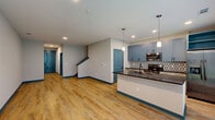 This two-story townhome in Titusville, Florida offers a thoughtfully designed layout spread across two floors. The ground level features an open-concept kitchen and living area, an attached garage with automatic opener, and multiple bathrooms. The kitchen is a standout space, showcasing blue-grey upper cabinetry, crisp white lower cabinets, a bold patterned tile backsplash, dark granite countertops on a central island with an undermount sink, pendant lighting, and a full suite of stainless steel appliances. Light wood-look flooring flows throughout the main living areas, complemented by teal accent baseboards and door frames that carry a consistent design theme throughout the home. The upper floor houses two bedrooms, including a generously sized primary bedroom, each fitted with plush carpet, ceiling fans, and window blinds. The bathrooms are finished with wood-look flooring, granite-topped vanities with light wood cabinetry, and tub-shower combinations. A dedicated laundry room on the upper level includes a full-size washer and dryer with overhead wire shelving. Two closets provide additional storage, one featuring built-in wire shelving systems. Natural light filters through slatted window blinds throughout, giving the home a bright and clean ambiance.