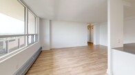 This well-appointed 2-bedroom, 1-bathroom unit offers a clean, modern aesthetic across a single floor. The open-concept layout seamlessly connects the living room and kitchen, creating a spacious and versatile living area. Large windows along the living room wall flood the space with natural light and provide views of the surrounding cityscape, enhancing the airy atmosphere throughout.

The kitchen is thoughtfully designed with white shaker cabinetry, dark countertops, a classic white subway tile backsplash, and a full suite of stainless steel appliances including a refrigerator, electric range, and over-the-range microwave. A peninsula with additional counter space extends into the open living area, making it ideal for both meal preparation and casual dining. Track lighting illuminates the kitchen efficiently.

Both bedrooms feature light hardwood-style flooring, bright white walls, and generous windows that bring in natural light. The primary bedroom includes a closet with a hanging rod. A hallway connects the bedrooms to the full bathroom, which is finished with white subway tile surrounding a soaker tub and shower combination. Light hardwood-style flooring runs consistently throughout the entire unit, contributing to its cohesive and contemporary feel.
