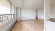 This well-appointed 2-bedroom, 1-bathroom unit offers a clean, modern aesthetic across a single floor. The open-concept layout seamlessly connects the living room and kitchen, creating a spacious and versatile living area. Large windows along the living room wall flood the space with natural light and provide views of the surrounding cityscape, enhancing the airy atmosphere throughout.

The kitchen is thoughtfully designed with white shaker cabinetry, dark countertops, a classic white subway tile backsplash, and a full suite of stainless steel appliances including a refrigerator, electric range, and over-the-range microwave. A peninsula with additional counter space extends into the open living area, making it ideal for both meal preparation and casual dining. Track lighting illuminates the kitchen efficiently.

Both bedrooms feature light hardwood-style flooring, bright white walls, and generous windows that bring in natural light. The primary bedroom includes a closet with a hanging rod. A hallway connects the bedrooms to the full bathroom, which is finished with white subway tile surrounding a soaker tub and shower combination. Light hardwood-style flooring runs consistently throughout the entire unit, contributing to its cohesive and contemporary feel.