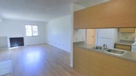 This single-floor residential space offers a clean, open-concept layout designed for comfortable everyday living. The living area is spacious and filled with natural light streaming in through a large window, creating a warm and airy atmosphere throughout. Light-toned hardwood flooring runs continuously across the main living space, lending a cohesive and polished look to the interior.

The kitchen features a practical pass-through design with wood-toned cabinetry and a countertop that opens directly to the living area, promoting an easy flow between spaces. A stainless steel sink is integrated into the countertop, and a full-size refrigerator is visible within the kitchen, indicating well-utilized functionality in a compact footprint.

The walls are finished in a clean white tone, complemented by a textured ceiling that adds subtle depth to the space. Electrical outlets are thoughtfully placed along the walls to support flexible furniture arrangements. The overall design is straightforward and functional, emphasizing openness and light. The neutral palette and simple finishes create a versatile backdrop well-suited to a variety of interior styles, making this a practical and inviting single-level living space.