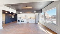 This thoughtfully designed single-floor unit blends contemporary finishes with an open, airy layout. Hardwood flooring flows throughout the space, complementing the contrast between crisp white walls and dark-toned ceilings and door frames that lend a bold, modern character.

The kitchen is a standout feature, outfitted with full-height white shaker cabinetry, a striking marble-veined backsplash and countertops, stainless steel appliances including a refrigerator and dishwasher, and an in-unit washer. Linear LED lighting above the kitchen zone adds a sleek, refined touch, while large windows allow natural light to pour in, offering views of the surrounding urban skyline.

The main living area is generously proportioned, with multiple tall windows framing sweeping city views and flooding the room with sunlight throughout the day. A distinctive slatted wood accent wall with integrated backlighting serves as a sophisticated design focal point.

The bedroom is well-sized with its own large window capturing urban vistas, and includes a dark-finished wardrobe with a mirrored panel for added functionality. Private corridor access and dark-panel doors throughout reinforce the space's cohesive modern aesthetic.

Overall, this unit offers a polished, urban living environment that balances clean minimalist design with warm, natural materials.