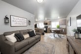 Located at 450 W Second S in Rexburg, Idaho, this 2-bedroom, 1-bathroom unit offers a well-designed single-level layout that maximizes its compact footprint. The open-concept living, dining, and kitchen area creates a cohesive, connected space anchored by light wood-style flooring throughout. The living room provides a comfortable gathering area with neutral walls and flush ceiling lighting, opening directly into the combined kitchen and dining zone.

The kitchen is a functional centerpiece, featuring a peninsula with a built-in sink, granite-style countertops, bar seating, and pendant lighting overhead. Medium-toned cabinetry lines the walls, complemented by black appliances including a refrigerator, range, and over-the-range microwave. A window above the counter brings in natural light. The adjacent dining area accommodates a round table and chairs alongside additional cabinetry for storage.

Both bedrooms are carpeted for comfort. The primary bedroom includes a closet with a hanging rod and a window with exterior views. The second bedroom also features closet storage. The shared full bathroom offers a tub-shower combination, wood-toned vanity with a granite-style countertop, and wood-style flooring, providing a clean, modern finish consistent with the rest of the unit.