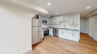 Located at 160 Seabury St in Fall River, MA, this two-bedroom, two-bathroom unit is thoughtfully laid out across two floors, making efficient use of its compact footprint. The main level houses the kitchen and primary living areas, while the upper floor accommodates additional rooms connected by a staircase and hallway.

The kitchen is a standout feature, showcasing gray shaker-style cabinetry, granite countertops, a white subway tile backsplash, and stainless steel appliances including a refrigerator, range, microwave, and dishwasher. Light hardwood flooring flows throughout both floors, lending warmth and visual continuity to the space.

Both bathrooms are finished to a consistent, modern standard, featuring gray vanities with granite countertops, hexagonal tile flooring, and clean white walls. One bathroom includes a glass-enclosed walk-in shower, while the other is equipped with a stacked washer and dryer unit for added convenience.

The bedrooms are simply appointed with neutral walls, hardwood floors, and gray-trimmed windows that bring in natural light. The primary bedroom, though compact, provides a functional layout. Overall, the unit presents a clean, contemporary aesthetic with updated finishes throughout.