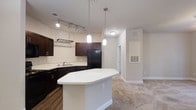 Located at 2030 Wildts Battery Blvd in Johns Island, South Carolina, this single-floor residence offers a thoughtfully designed open-concept layout that seamlessly connects the kitchen and living areas. The kitchen is a standout feature, showcasing rich dark cabinetry that contrasts beautifully against light-colored walls and a generous white countertop island, ideal for meal preparation or casual dining. A combination of track lighting and elegant pendant lights provides layered illumination, creating a bright and functional cooking space. Black appliances, including a full-size refrigerator, complement the dark cabinetry for a cohesive aesthetic. Durable hardwood-style flooring grounds the kitchen area, while plush carpeting flows into the adjacent living space, adding warmth and comfort underfoot. The open sightlines between rooms enhance the sense of spaciousness, while neutral wall tones provide a versatile backdrop for a variety of interior styles. Vented HVAC registers are thoughtfully positioned throughout, ensuring year-round comfort. The overall ambiance is clean, modern, and move-in ready, making this Johns Island residence a well-appointed and inviting place to call home.