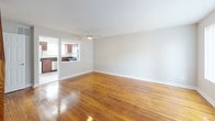 This two-floor space offers a well-organized layout with consistent finishes throughout. The main level features a generously sized living area with gleaming hardwood floors, neutral gray walls, and a ceiling fan that promotes airflow and comfort. A large window with vertical blinds allows natural light to fill the room, which connects openly to the kitchen. A staircase along one wall leads to the upper floor, adding architectural dimension to the space.

The kitchen is efficiently designed, equipped with rich cherry wood cabinetry, dark granite countertops, and a full suite of stainless steel appliances, including a gas range, over-the-range microwave, and refrigerator. The layout maximizes counter space and storage, making it functional for everyday use.

The upper floor hosts multiple rooms, each featuring the same warm hardwood flooring, neutral walls, and ceiling fans. Vaulted ceilings in the bedrooms enhance the sense of space, while windows fitted with horizontal blinds provide natural light and privacy. Built-in closet storage is visible in at least one room.

The bathroom features floor-to-ceiling white square tile with black accent trim and hardware, paired with a soaking tub, giving it a classic, timeless aesthetic. Overall, the space maintains a clean and cohesive character across both floors.