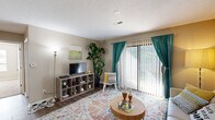 This efficiently designed two-bedroom unit offers a well-organized single-floor layout that maximizes every square foot of its living space. The living room serves as the heart of the unit, featuring rich hardwood-style flooring, a textured ceiling, and a large sliding glass door dressed with teal drapes and vertical blinds that flood the room with natural light and provide views of the surrounding greenery outside.

The kitchen is equipped with light wood cabinetry, dark countertops, and a full suite of black appliances, including a refrigerator, range, microwave, and dishwasher. Adjacent to the kitchen, the dedicated dining area features wood-style flooring and overhead lighting, providing a defined space for meals.

The primary bedroom is a generously sized retreat with plush carpeting, a ceiling fan with light fixture, and a window with outdoor views. It offers ample space for full bedroom furnishings. The second bedroom also features carpet flooring, a ceiling fan, and a window, making it a comfortable and versatile room suitable for sleeping or use as a home office.

Throughout the unit, neutral warm-beige walls provide a clean, cohesive backdrop. The layout flows intuitively, connecting living, dining, kitchen, and sleeping areas with ease.