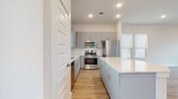 This two-story home showcases a clean, contemporary design highlighted by a neutral palette and quality finishes throughout. The open-concept main level seamlessly connects the living area and kitchen, creating a generous, light-filled space. Large windows fitted with blinds invite abundant natural light, while light wood-tone flooring and a ceiling fan contribute to a comfortable, airy atmosphere. A staircase leads to the upper level, reinforcing the home's functional two-floor layout.

The kitchen is a standout feature, designed with grey shaker-style cabinetry, brushed gold hardware, and crisp white quartz countertops. A central island provides additional prep and seating space. Stainless steel appliances — including a gas range, over-the-range microwave, and refrigerator — are complemented by a white subway tile backsplash, lending the kitchen a polished, modern character.

The bathrooms are finished with striking marble-look porcelain tile flooring throughout. A full bathroom on the upper level features a glass-enclosed walk-in shower, grey vanity cabinetry, and a window for natural light. A second full bathroom includes a tub-shower combination with matching marble-style wall tile. A dedicated water closet with the same tile flooring provides additional convenience.