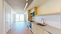 Located at 39 Bruton Street in San Francisco's Yerba Buena Island neighborhood, this thoughtfully designed one-bedroom, one-bathroom residence offers a streamlined modern aesthetic throughout. The open-plan kitchen and living area serves as the heart of the home, featuring a sleek galley-style kitchen appointed with light wood cabinetry, a white subway tile backsplash, stainless steel appliances including a range, microwave, and refrigerator, and a single-basin sink with a contemporary faucet. Warm light wood-tone flooring runs continuously through the space, complementing the clean, neutral palette. Recessed and linear ceiling lighting provides a polished finish alongside the exposed concrete ceiling elements that add an industrial character. Floor-to-ceiling windows flood the living area with natural light and frame sweeping views of the San Francisco Bay and downtown skyline — a true standout feature of this residence. The bedroom is a bright, serene retreat with its own large window showcasing the same breathtaking bay and city views, complemented by built-in closet storage. Two closets offer generous storage options. The bathroom is finished in crisp white tile with a soaking tub, shower, and light wood vanity. In-unit laundry completes this well-appointed home.