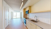 Located at 39 Bruton Street in San Francisco's Yerba Buena Island neighborhood, this thoughtfully designed one-bedroom, one-bathroom residence offers a streamlined modern aesthetic throughout. The open-plan kitchen and living area serves as the heart of the home, featuring a sleek galley-style kitchen appointed with light wood cabinetry, a white subway tile backsplash, stainless steel appliances including a range, microwave, and refrigerator, and a single-basin sink with a contemporary faucet. Warm light wood-tone flooring runs continuously through the space, complementing the clean, neutral palette. Recessed and linear ceiling lighting provides a polished finish alongside the exposed concrete ceiling elements that add an industrial character. Floor-to-ceiling windows flood the living area with natural light and frame sweeping views of the San Francisco Bay and downtown skyline — a true standout feature of this residence. The bedroom is a bright, serene retreat with its own large window showcasing the same breathtaking bay and city views, complemented by built-in closet storage. Two closets offer generous storage options. The bathroom is finished in crisp white tile with a soaking tub, shower, and light wood vanity. In-unit laundry completes this well-appointed home.